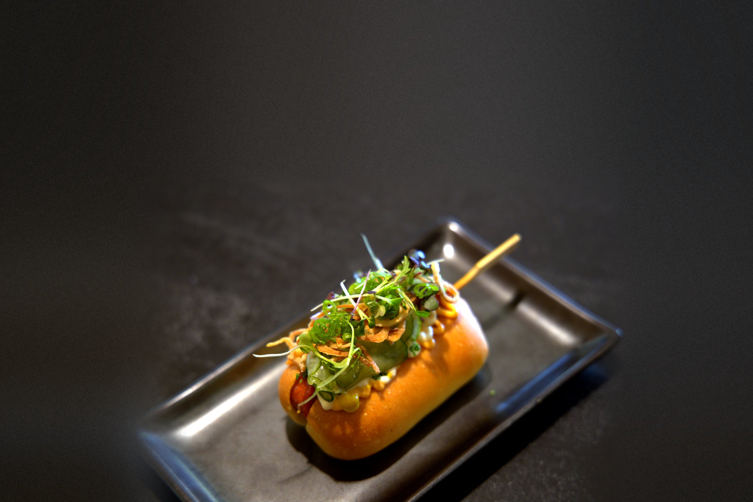 Chef Taus's gourmet Danish-style hot dog in a brioche bun with microgreens, on a dark slate tray